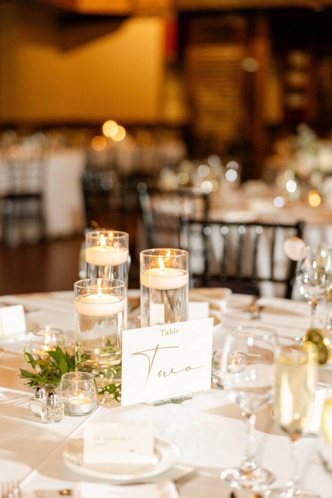 a table set for a wedding featuring one of our Fishermen's Inn Rentals: glass cylinders with floating candles creating a warm, inviting atmosphere.