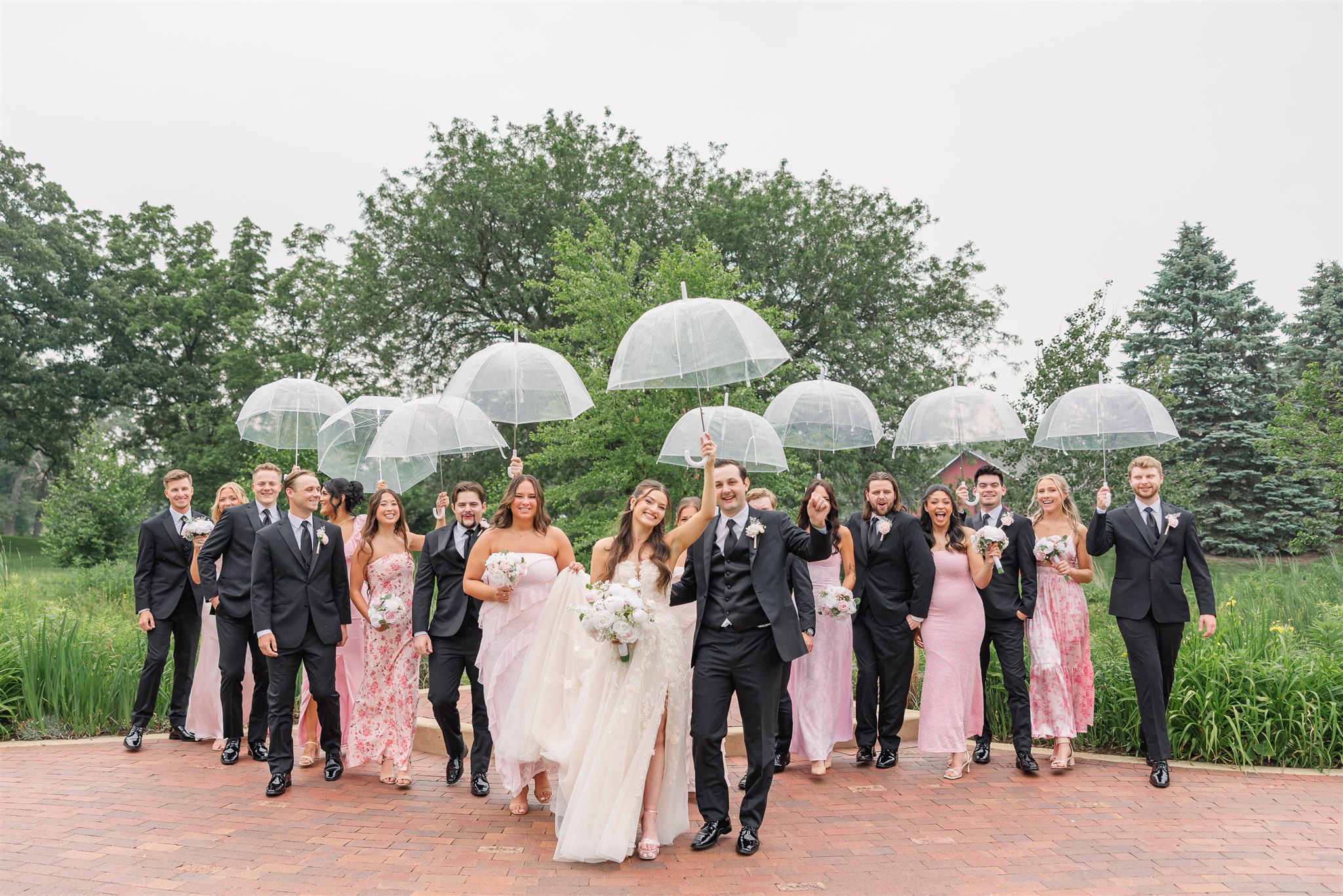 The bridal party with clear umbrellas posing in the rain.