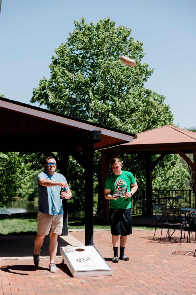 Groom and groomsmen enjoying pre-wedding time playing bags and having a beer on the patio | Friday Weddings at Fishermen's Inn