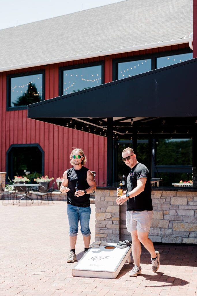 Groom and groomsmen enjoying pre-wedding time playing bags and having a beer on the patio | Friday Weddings at Fishermen's Inn