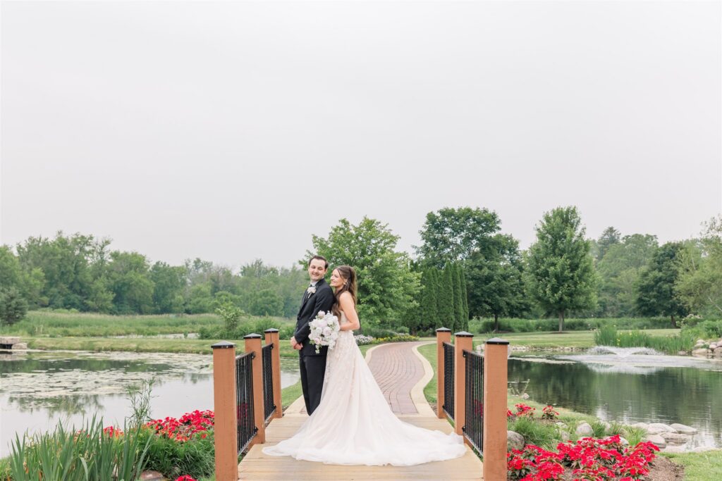 The bride and groom pose on the bridge on the grounds of Fishermen's Inn surrounded by ponds and beautiful red flowers.