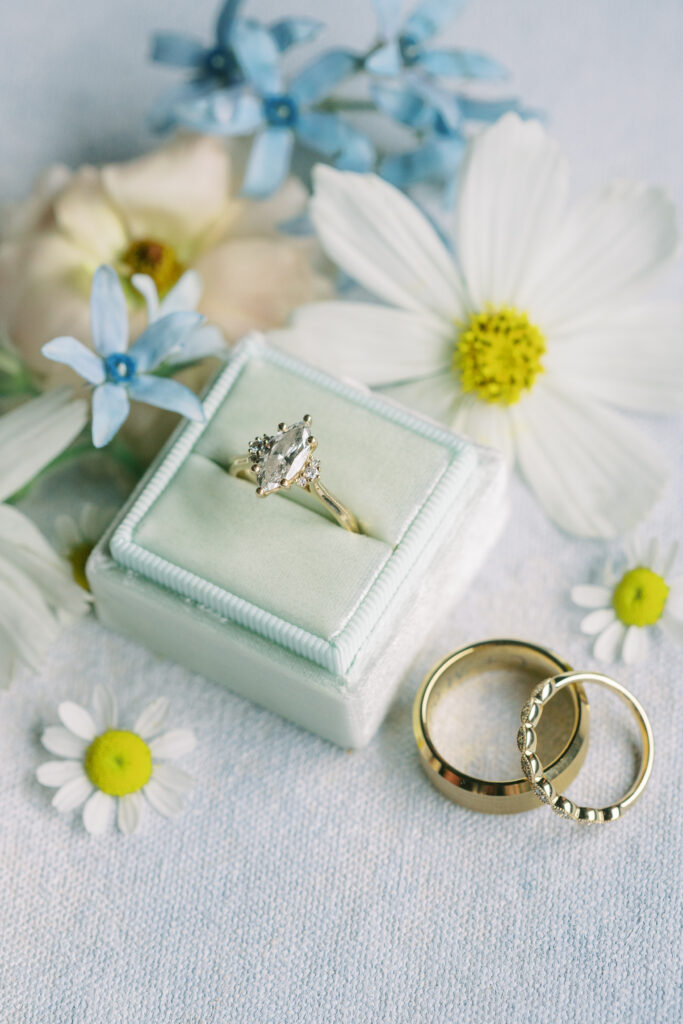 Wedding rings displayed with blue and white flowers in a velvet ring box before a June wedding at Fishermen's Inn in Elburn, Illinois.