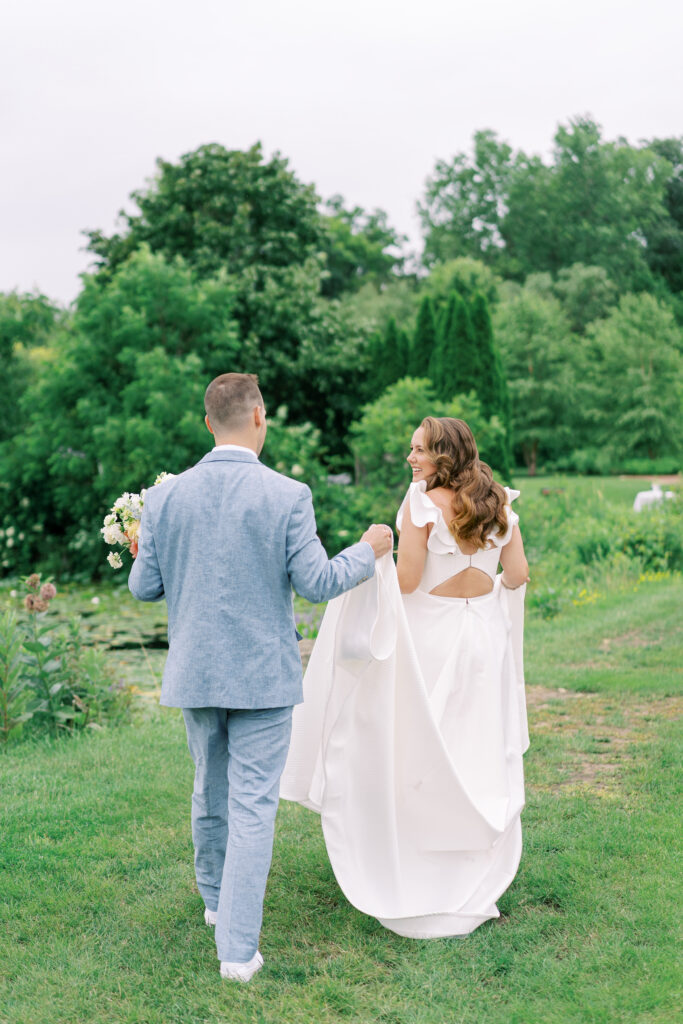 Bride and groom walking hand in hand beside the pond during their summer wedding at Fishermen's Inn in Elburn, Illinois.