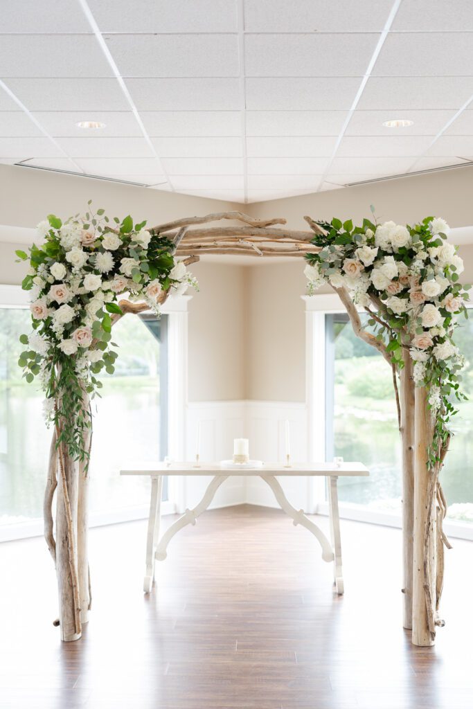 Wooden arch and pastel florals and greenery decorating the ceremony space at Fishermen’s Inn