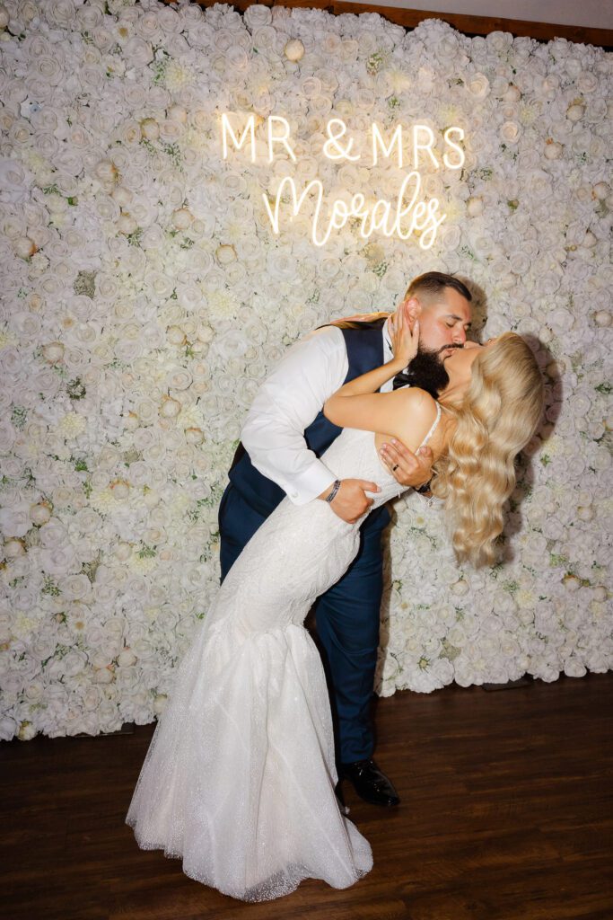 Linda and Ricky sharing a kiss in front of the floral wall at their Fishermen’s Inn wedding