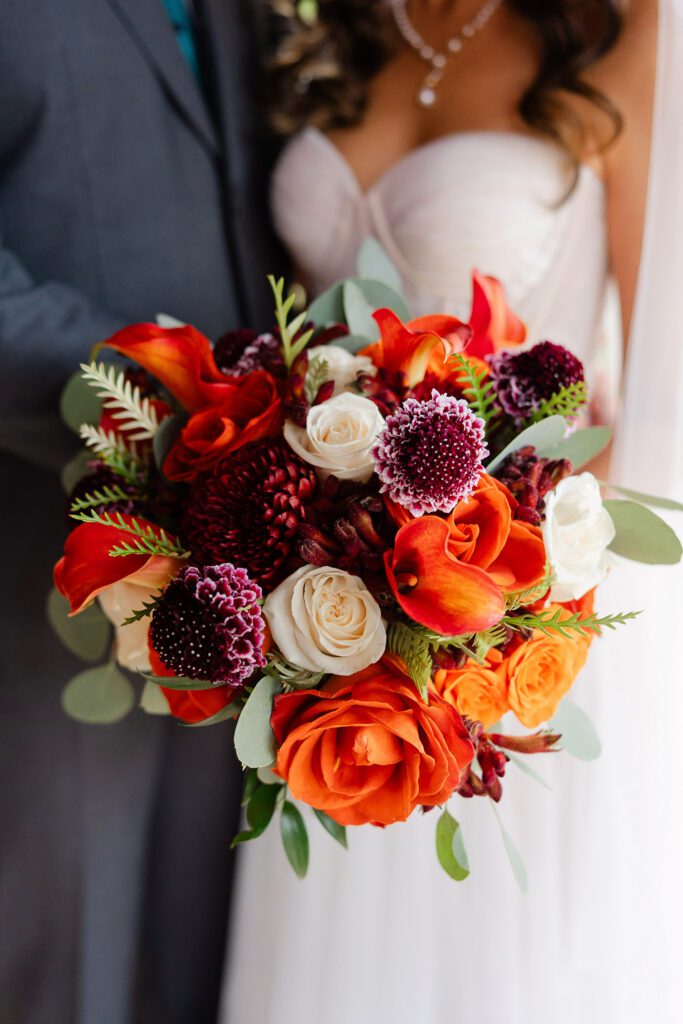 Close-up of Tina’s colorful fall wedding bouquet with red, orange, pink and burgundy flowers.