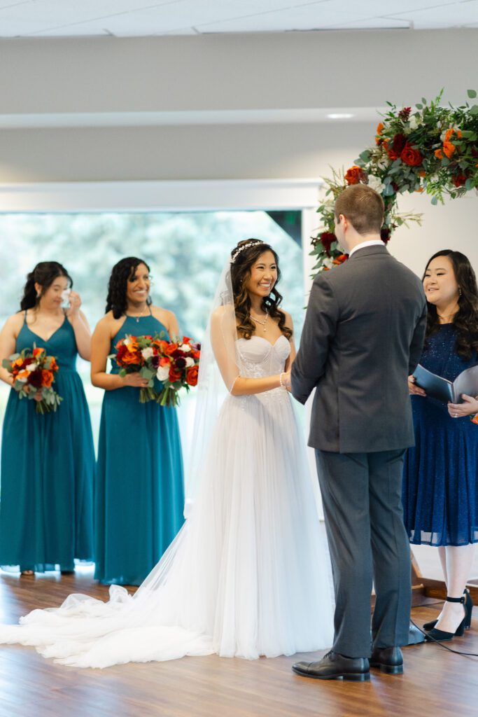 Tina and Connor stand beneath the floral arch during their indoor wedding ceremony.