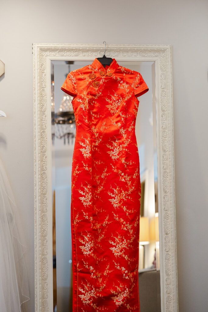 Tina’s red Chinese wedding dress with gold floral embroidery hangs beside a window.