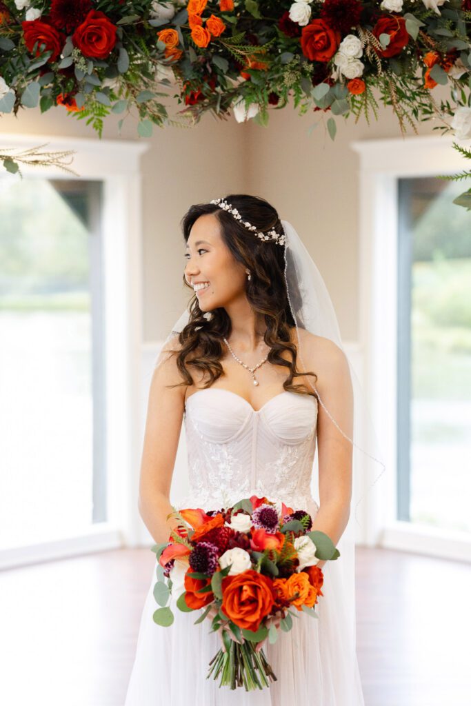 Tina holds her vibrant fall bouquet beneath a colorful floral ceremony arch.